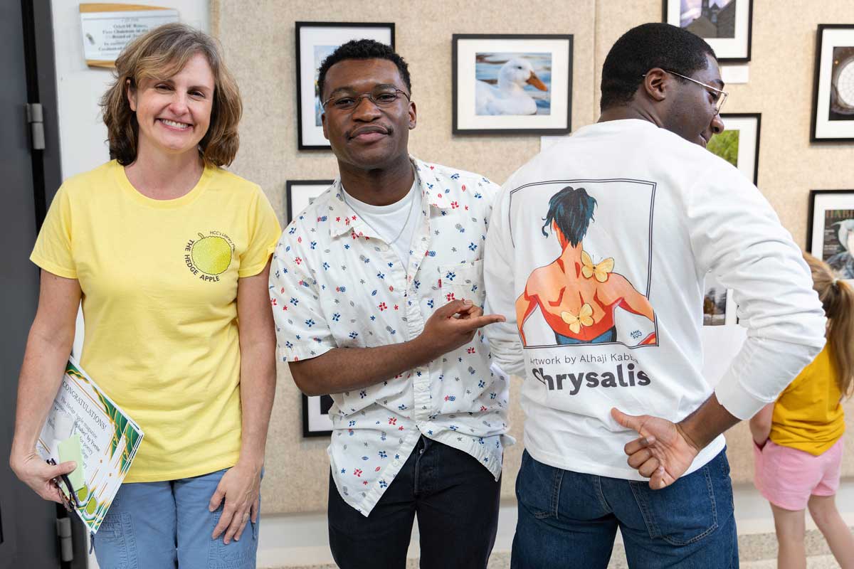 An English instructor standing with two students while one points to the design on the other's shirt