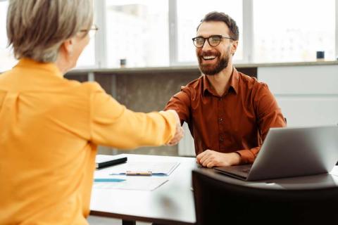 An interviewer sitting at a desk, shaking the hand of a potential employee